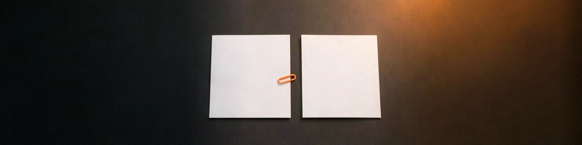 Photograph of two blank sheets of paper side by side, with an orange paper clip on the edge of the left one