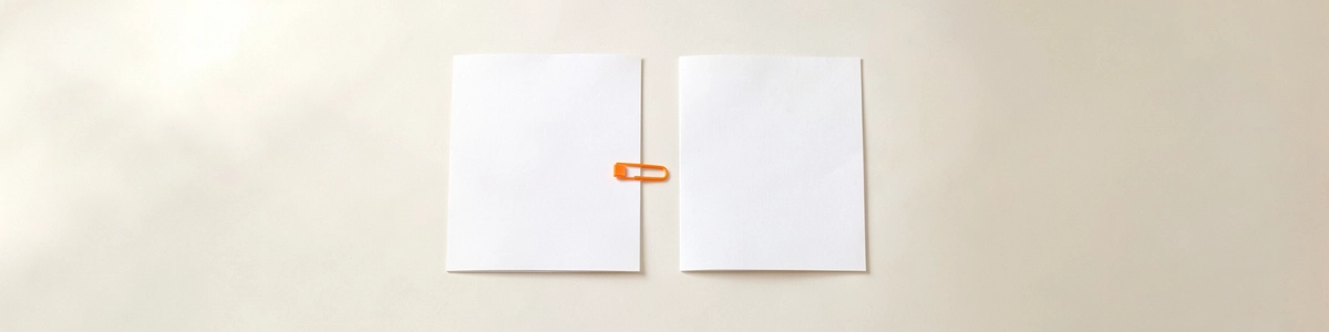 Photograph of two blank sheets of paper side by side, with an orange paper clip on the edge of the left one