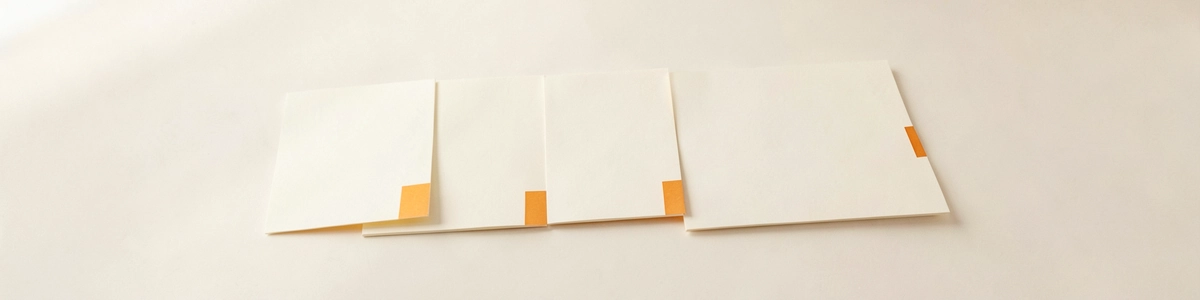 Photograph of four blank sheets of paper laid out in a row like steps, with small tabs at their edges
