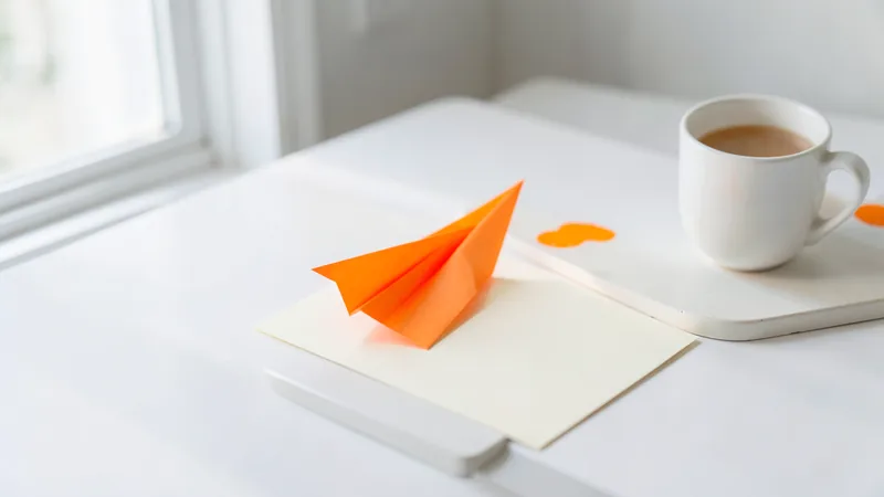 Photograph of an orange paper airplane on a blank card