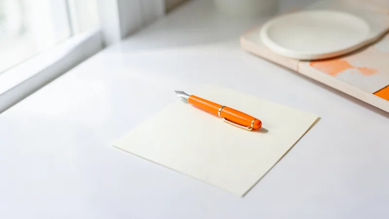 Photograph of an orange fountain pen on a blank cream card